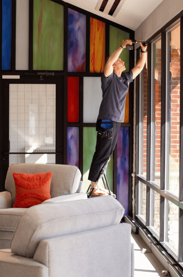 man installs curtains on muti-panel window with stained glass in background